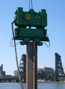 Free-hanging vibratory pile driver driving a CAZ box-pile.